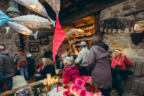 People sitting in a stone building decorated with papier mache fish with one woman holding a violin bow and others greeting each other