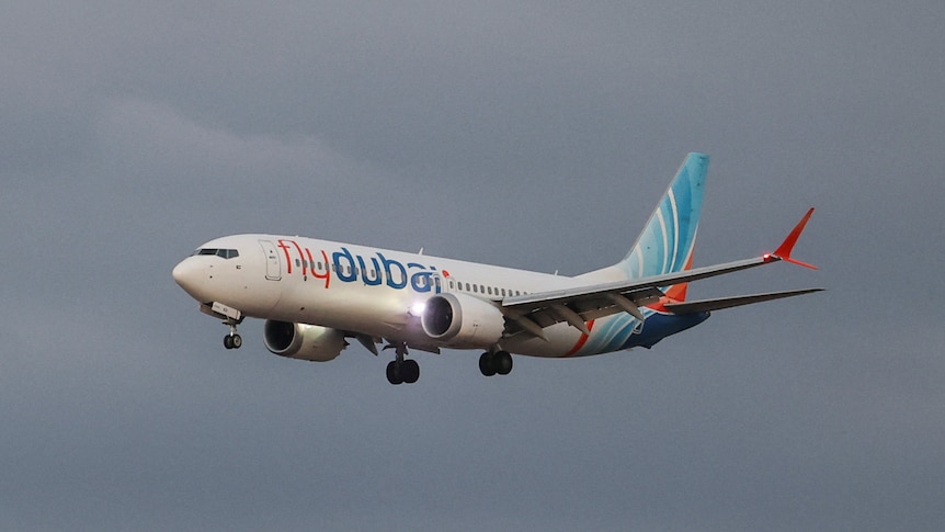 A white, blue and orange flydubai Boeing 737 aircraft flies against an overcast sky
